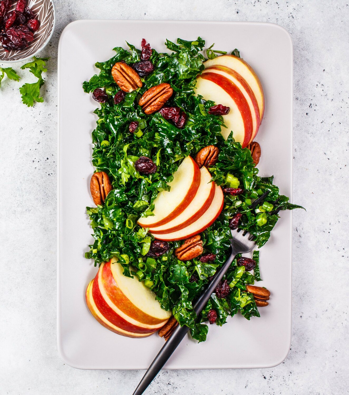 Healthy vegan salad with apple, cranberry, kale and pecan in a rectangular plate, top view.
